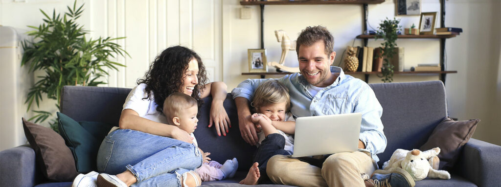 family laughing on a couch with a laptop computer as a they review the Haller hvac summer maintenance checklist