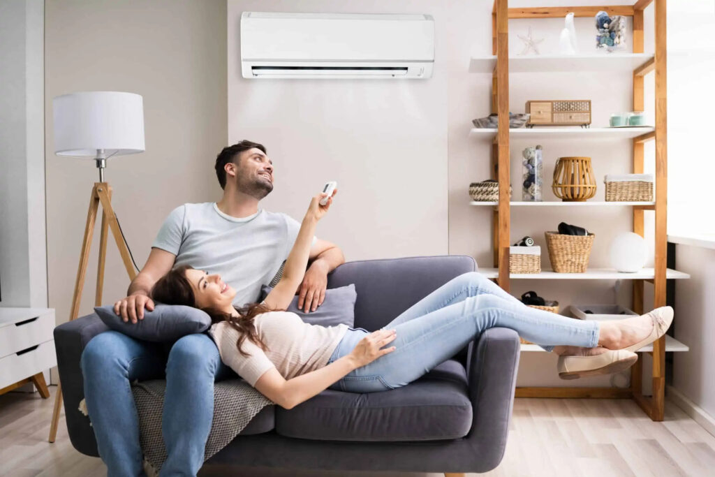 A couple relaxes on the couch under a ductless mini-split cooling system.