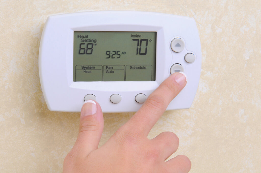 Closeup of a woman's hand setting the room temperature on a modern programable thermostat.