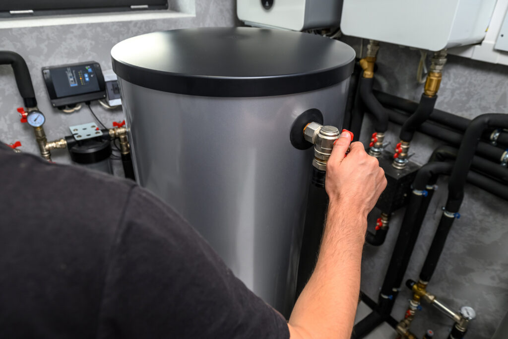 Plumber's hand on a modern electric water heater located in a home.