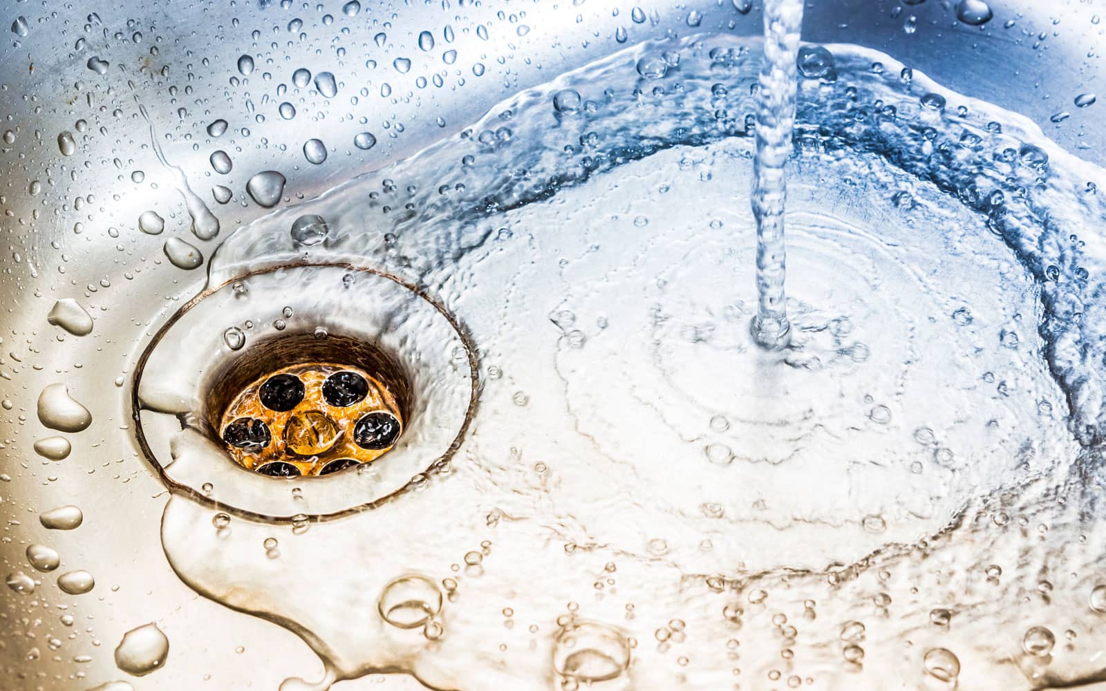Water running into a clean stainless steel sink and down the drain