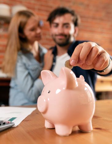 Happy couple putting coin into pink piggy bank